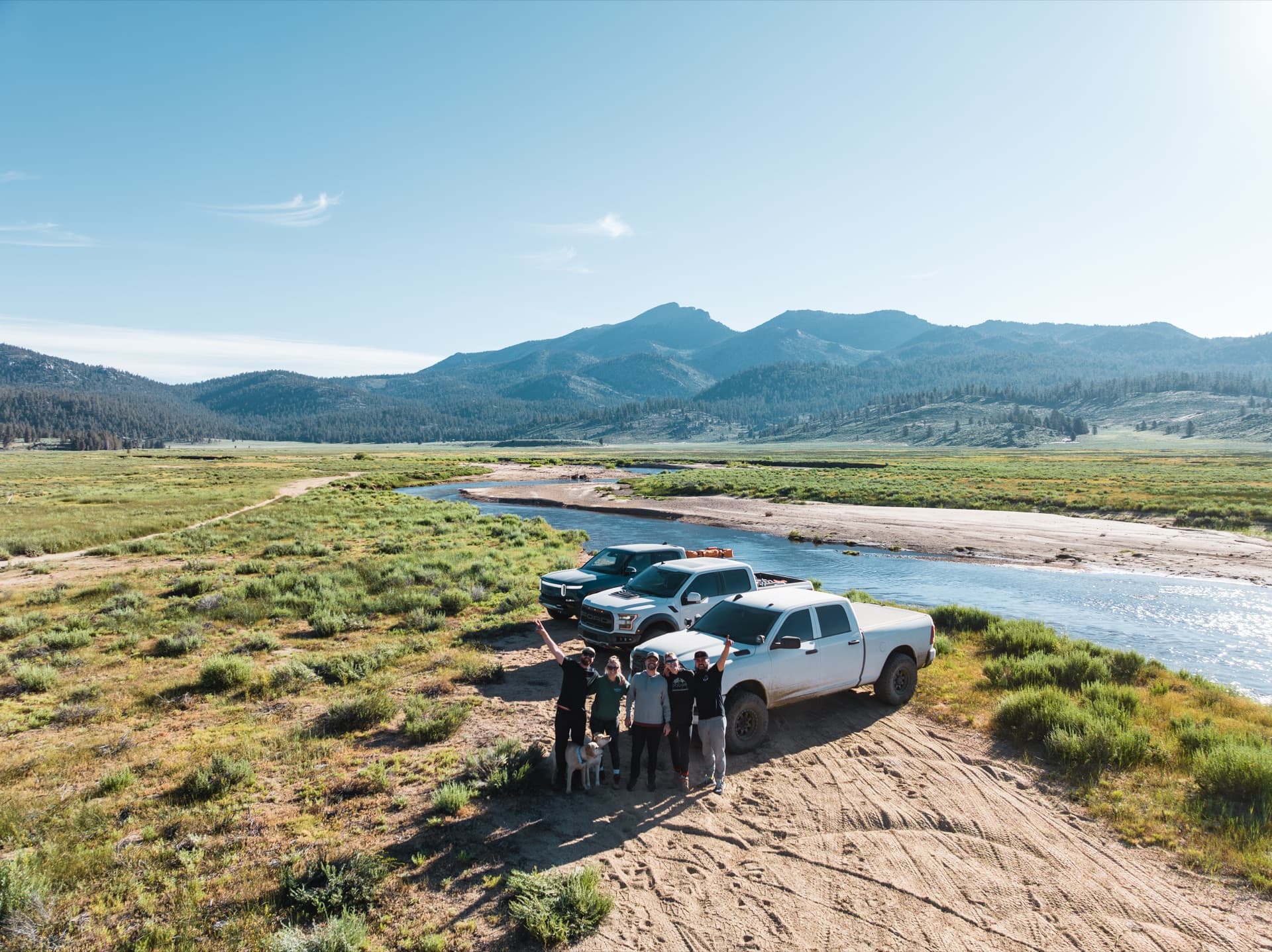The Overland Story crew with trucks by the river in a mountain valley